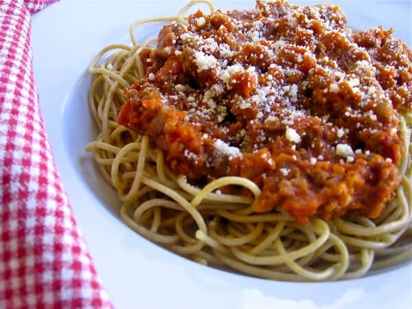 Slow Cooker Sausage Spaghetti Sauce over cooked spaghetti in a white bowl with red checkered napkin