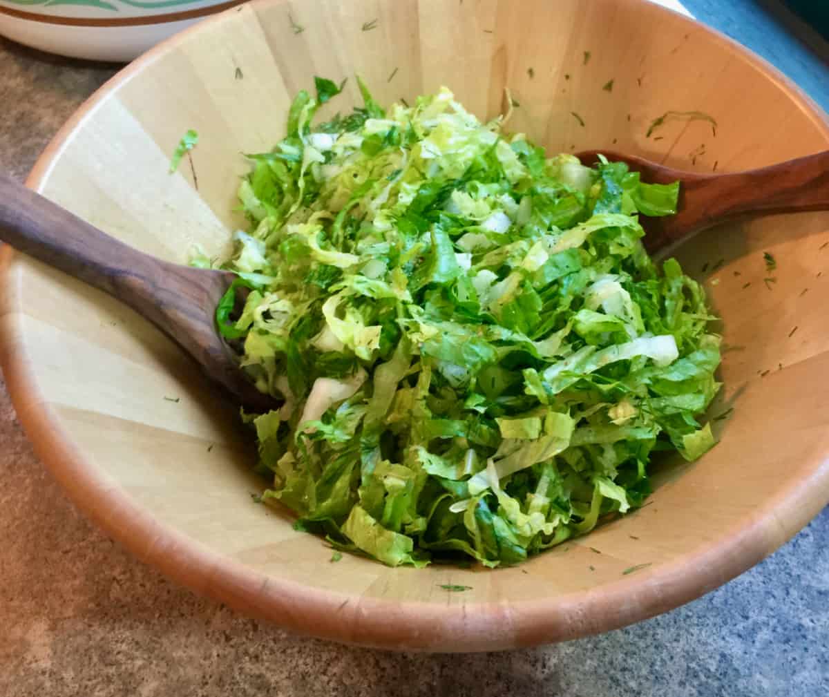 Shredded romaine salad with dill in wooden salad bowl.