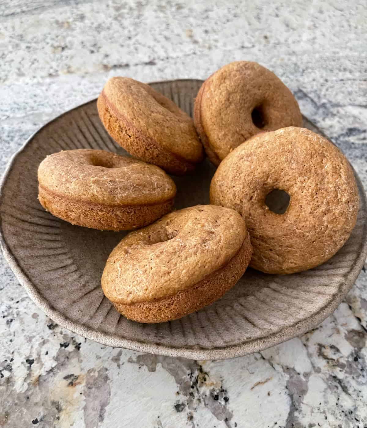 Fresh baked whole wheat donuts on ceramic serving platter on granite.