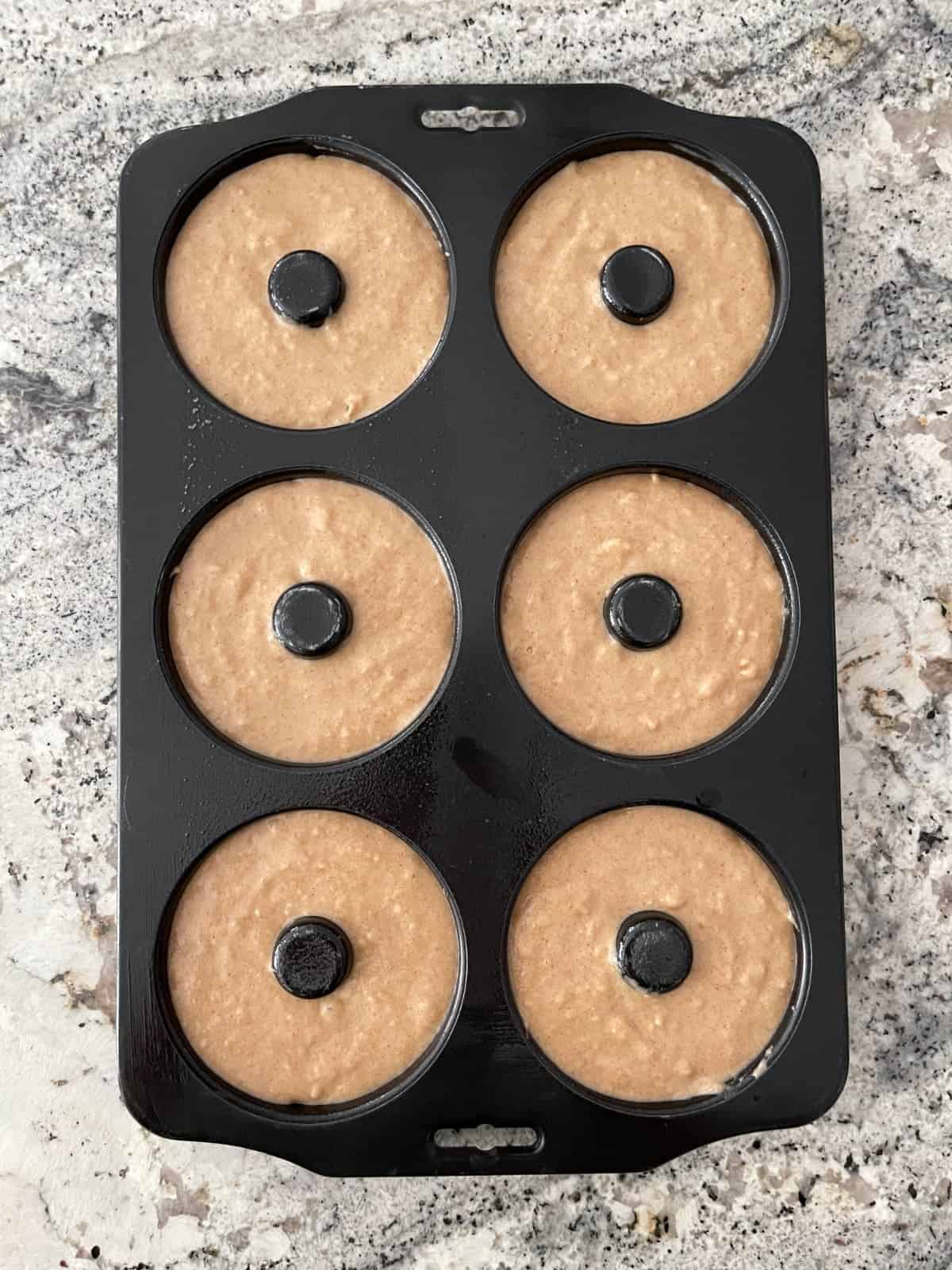 Unbaked whole wheat donuts in baking pan on granite counter.