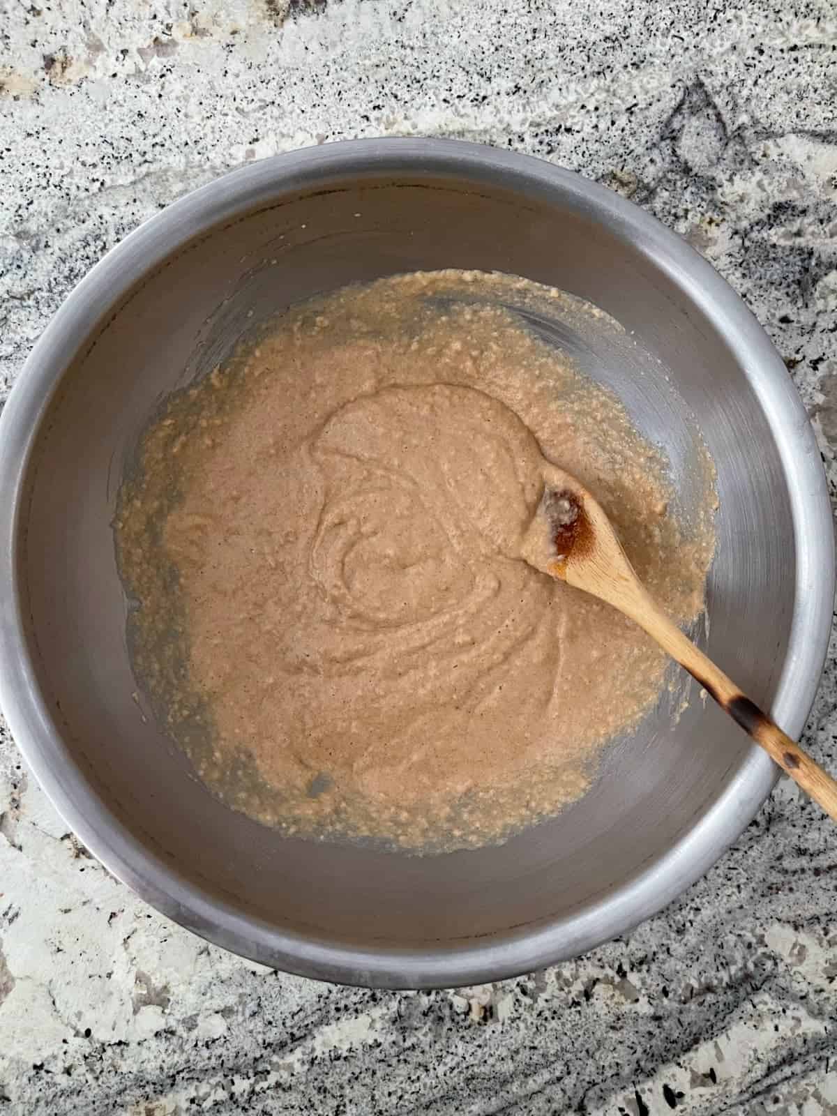 Mixing whole wheat donut batter with wooden spoon in mixing bowl.