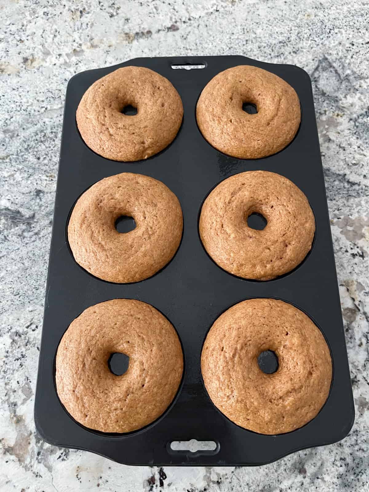 Fresh baked whole wheat donuts cooling in pan on granite counter.