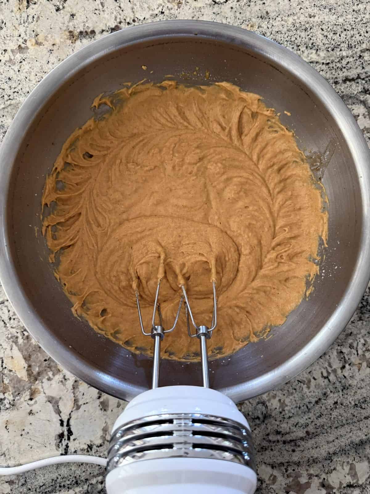 Beating pumpkin muffin batter in mixing bowl with handheld electric mixer.