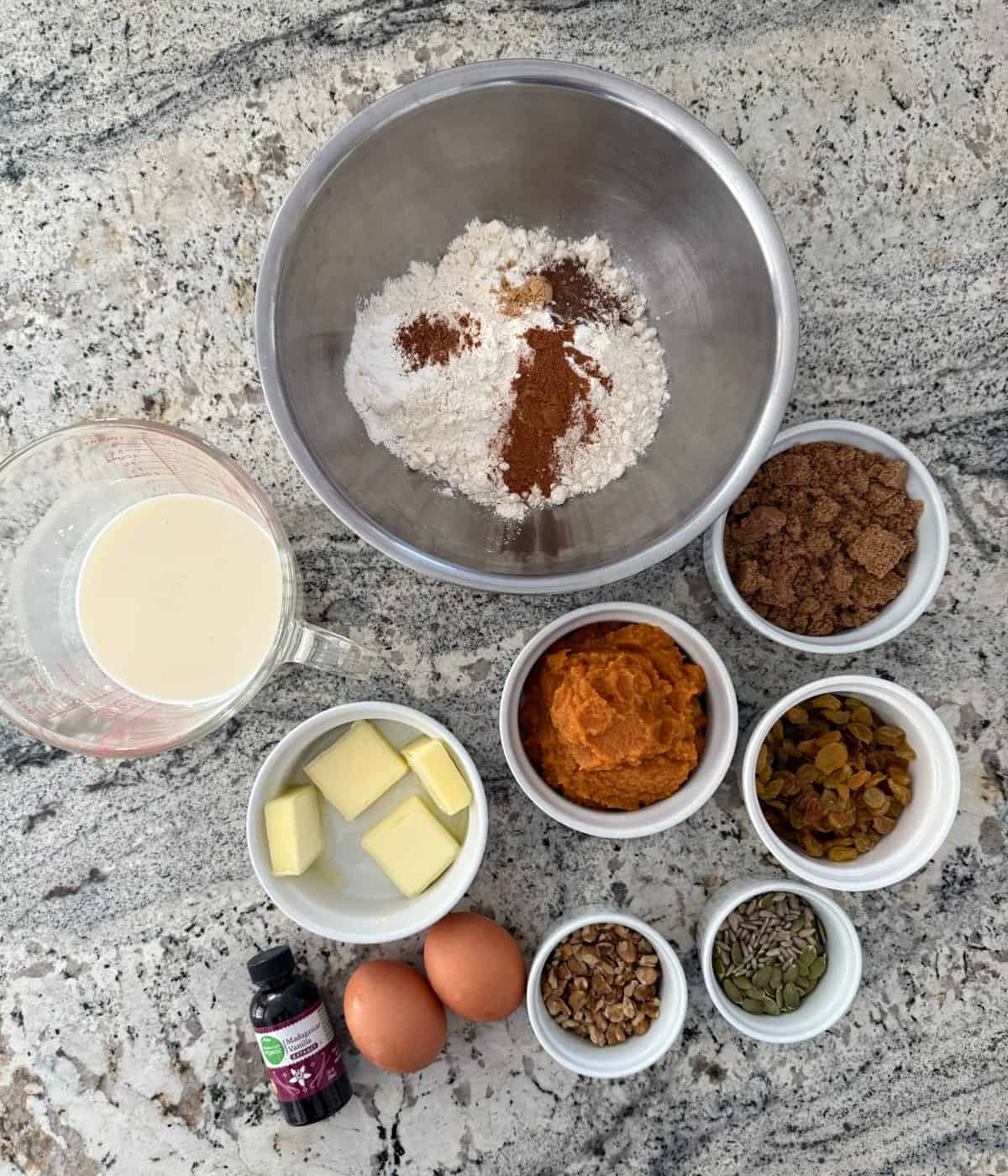 Ingredients for making pumpkin muffins, including: flour, cinnamon, buttermilk, butter, pumpkin puree, brown sugar, golden raisins, eggs, vanilla, walnuts, pumpkin and sunflower seeds.