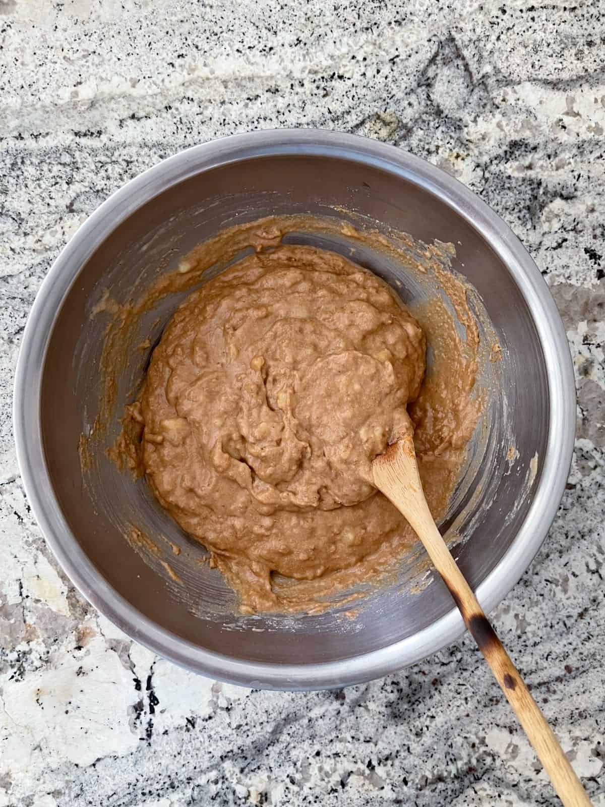 Mixing banana mocha muffin batter in bowl with wooden spoon.
