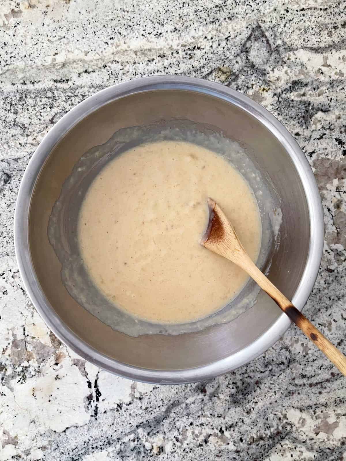 Mixing butter, sweetener, egg, vanilla, yogurt and mashed banana in mixing bowl with wooden spoon.