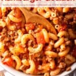 Hamburger goulash with tomatoes and elbow macaroni in serving dish with wooden spoon.