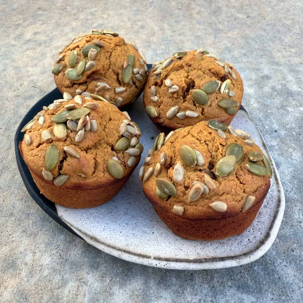 Fresh baked pumpkin muffins topped with sunflower and pumpkin seeds on ceramic plate.