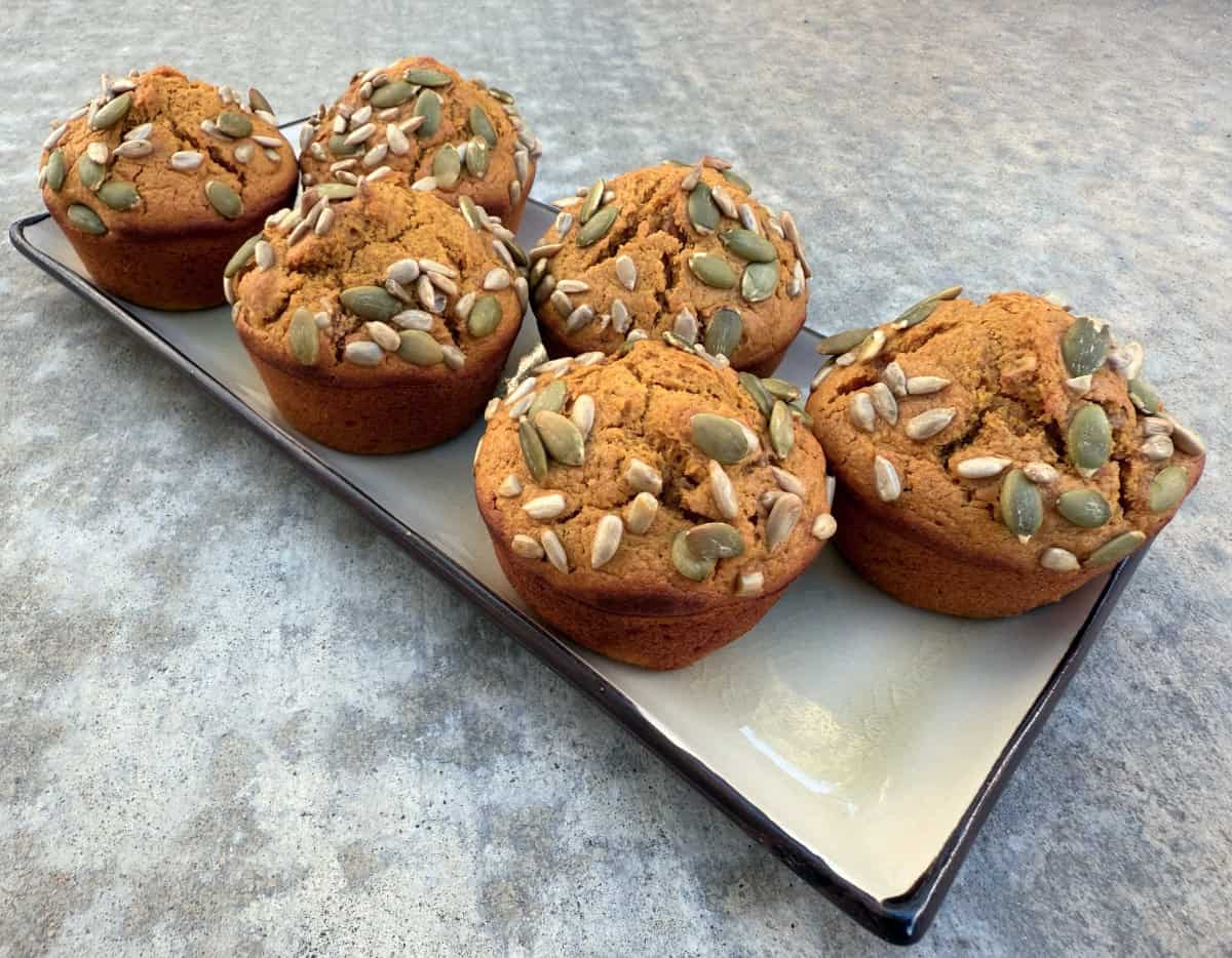 Fresh baked pumpkin muffins topped with pumpkin and sunflower seeds on serving platter.