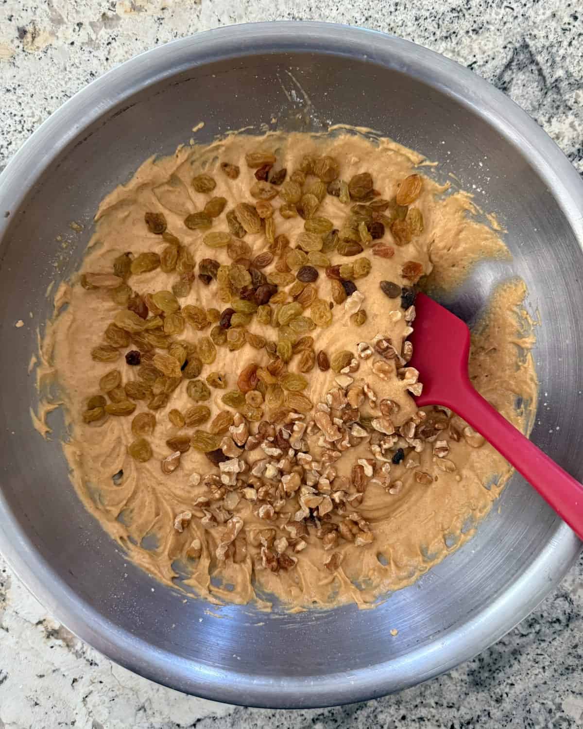 Folding golden raisins and chopped walnuts into pumpkin muffin batter with rubber spatula.