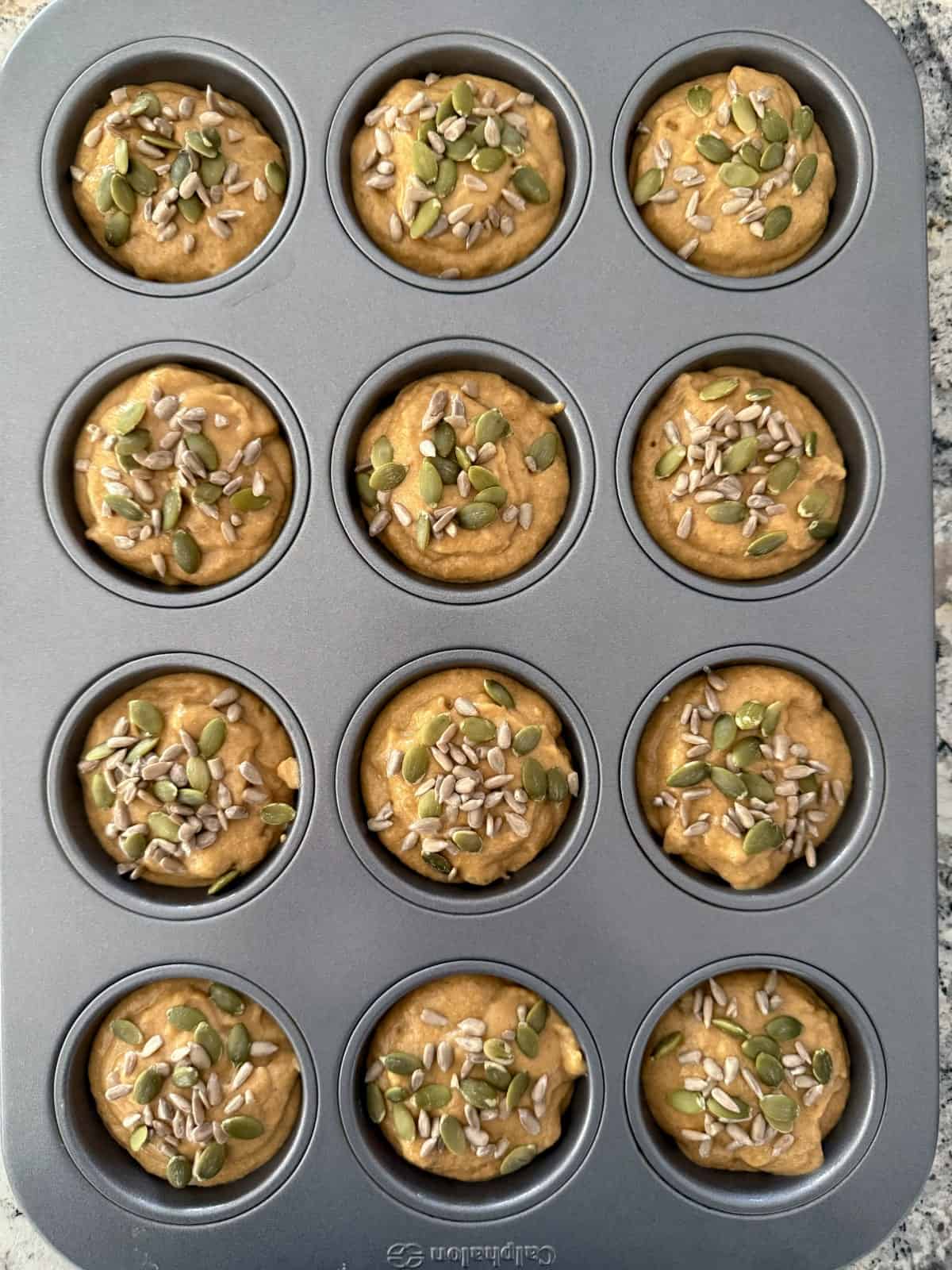Unbaked pumpkin muffins topped with pumpkin and sunflower seeds in standard 12-cup muffin pan.