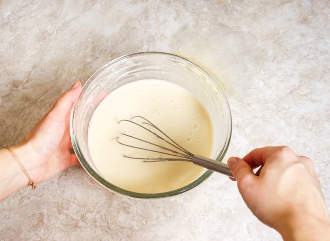 Woman's hands whisking confectioner's sugar and cream in a glass bowl for cookie icing