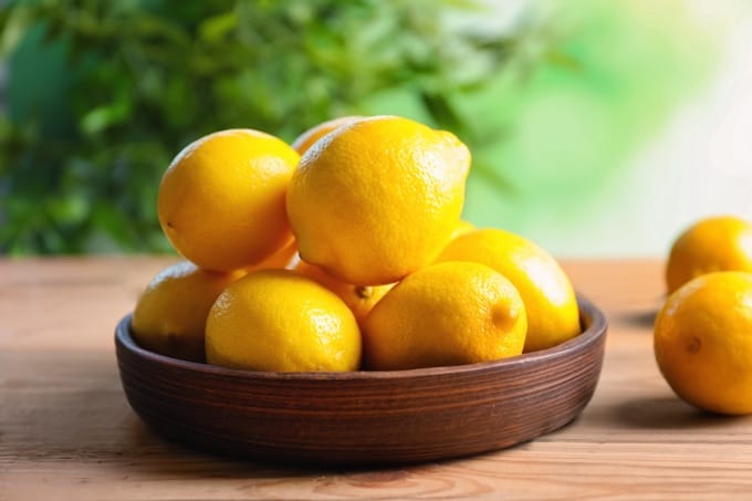 Shallow wooden bowl with ripe lemons on wood table against blurred background