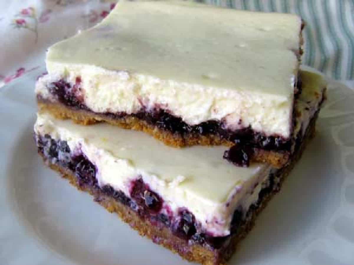 Two blueberry cheesecake bars stacked on a small white plate.