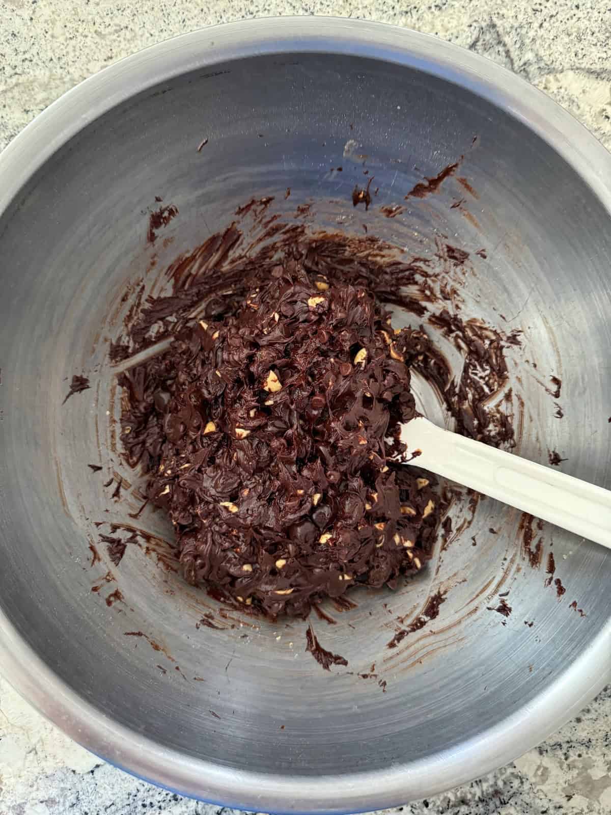 Stirring together chunky chocolate cookie dough in stainless mixing bowl with spatula.