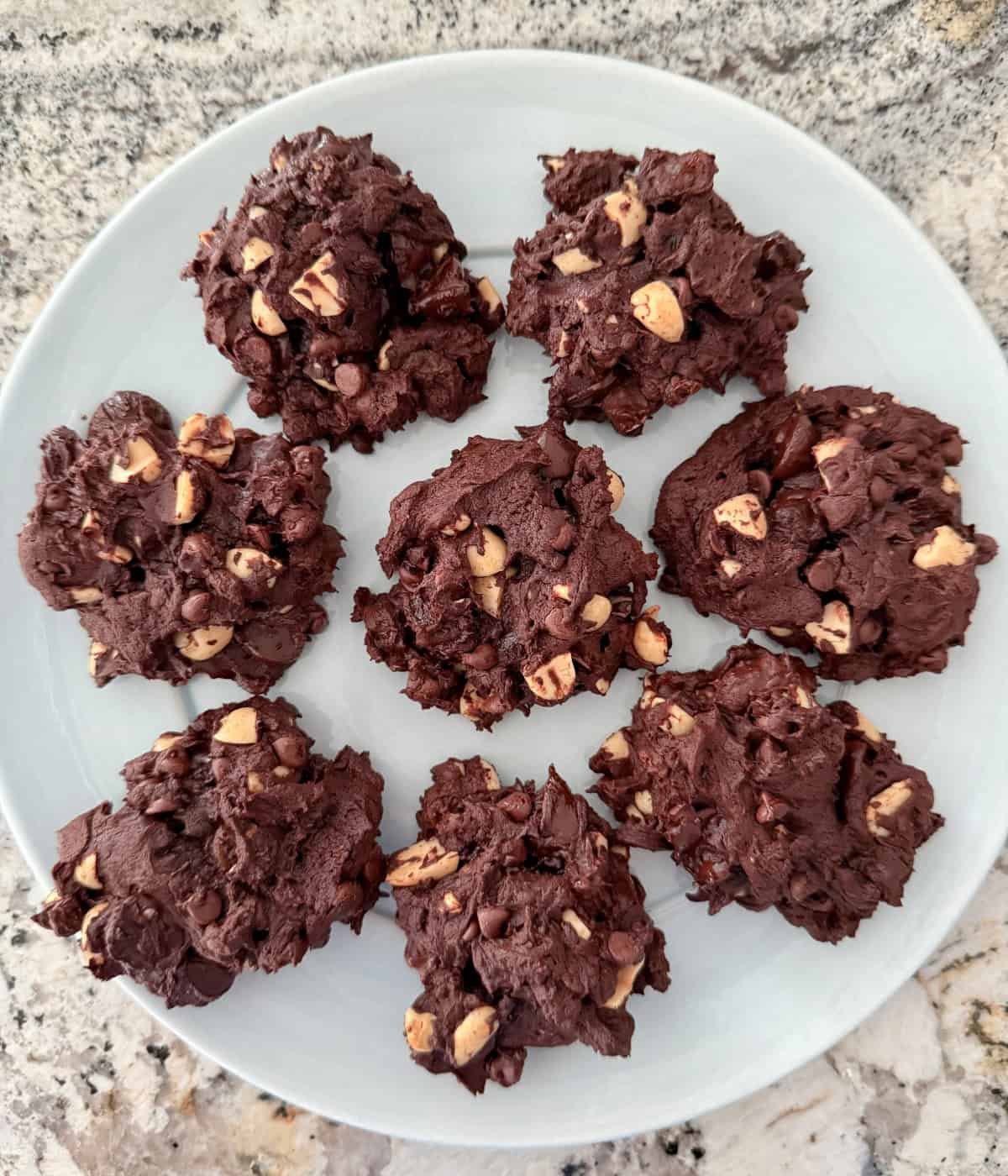 Chunky chocolate cookies with peanuts and raisins on round plate.