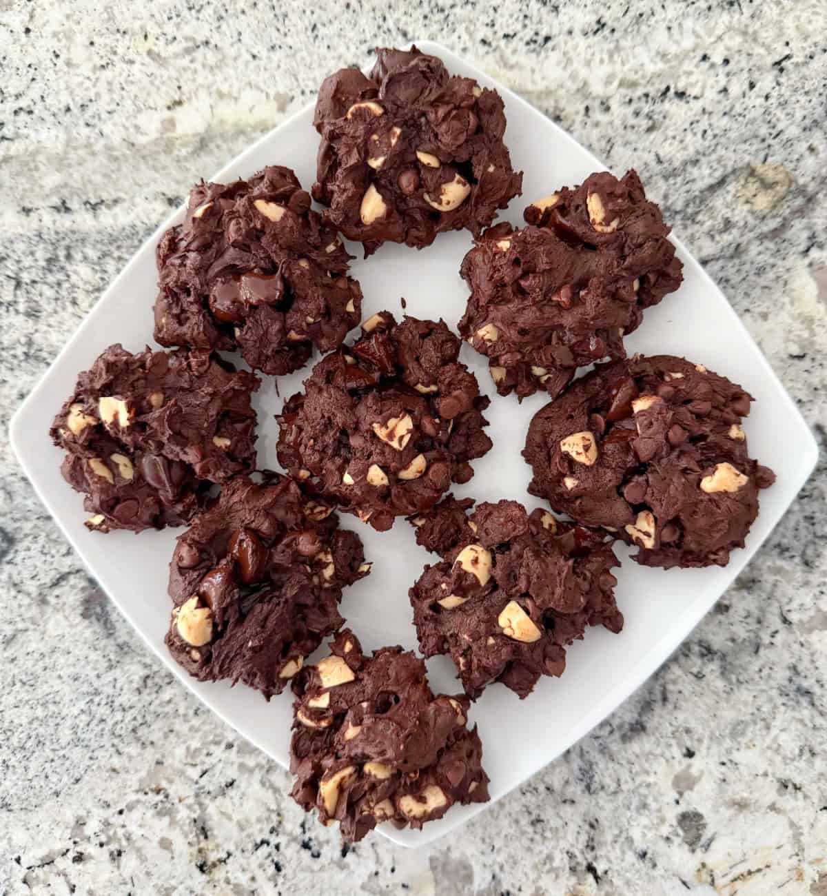 Chunky chocolate cookies with raisins and peanuts on white plate.