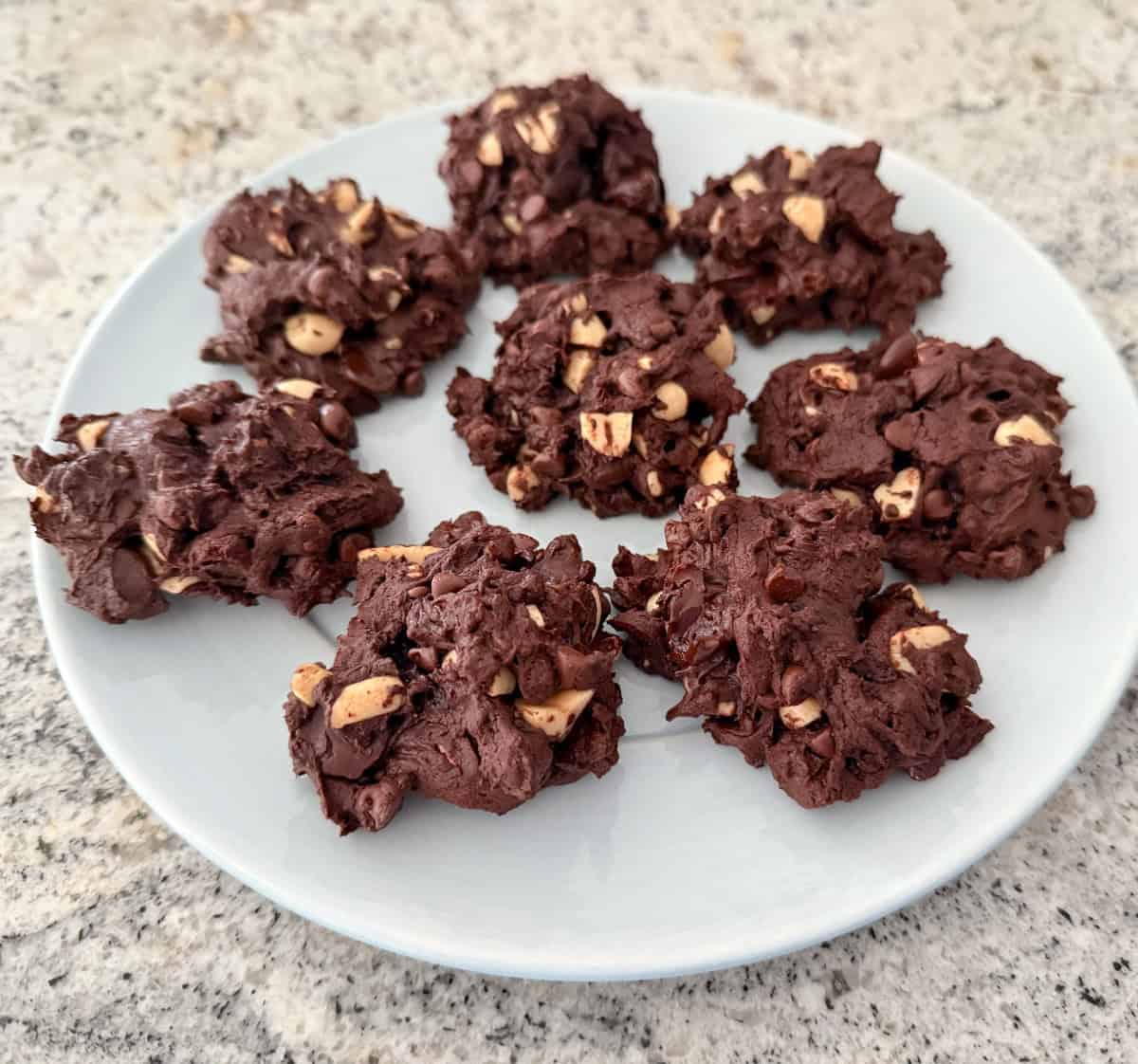 Chunky chocolate cookies with peanuts and raisins on small round plate.