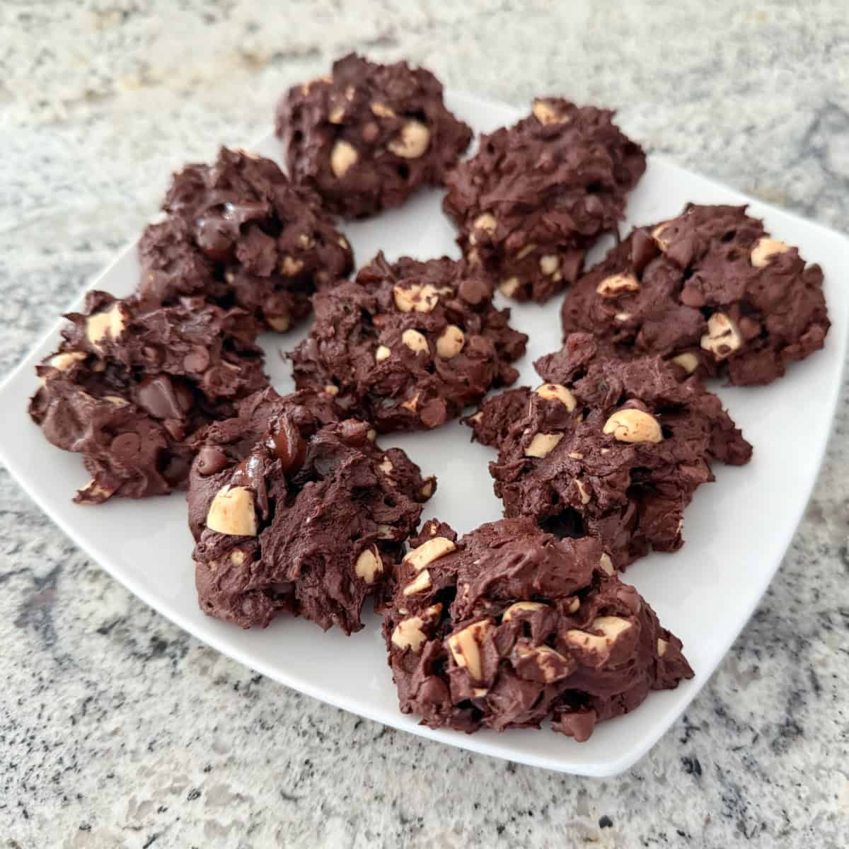 Chunky chocolate cookies with raisins and peanuts on square white plate.