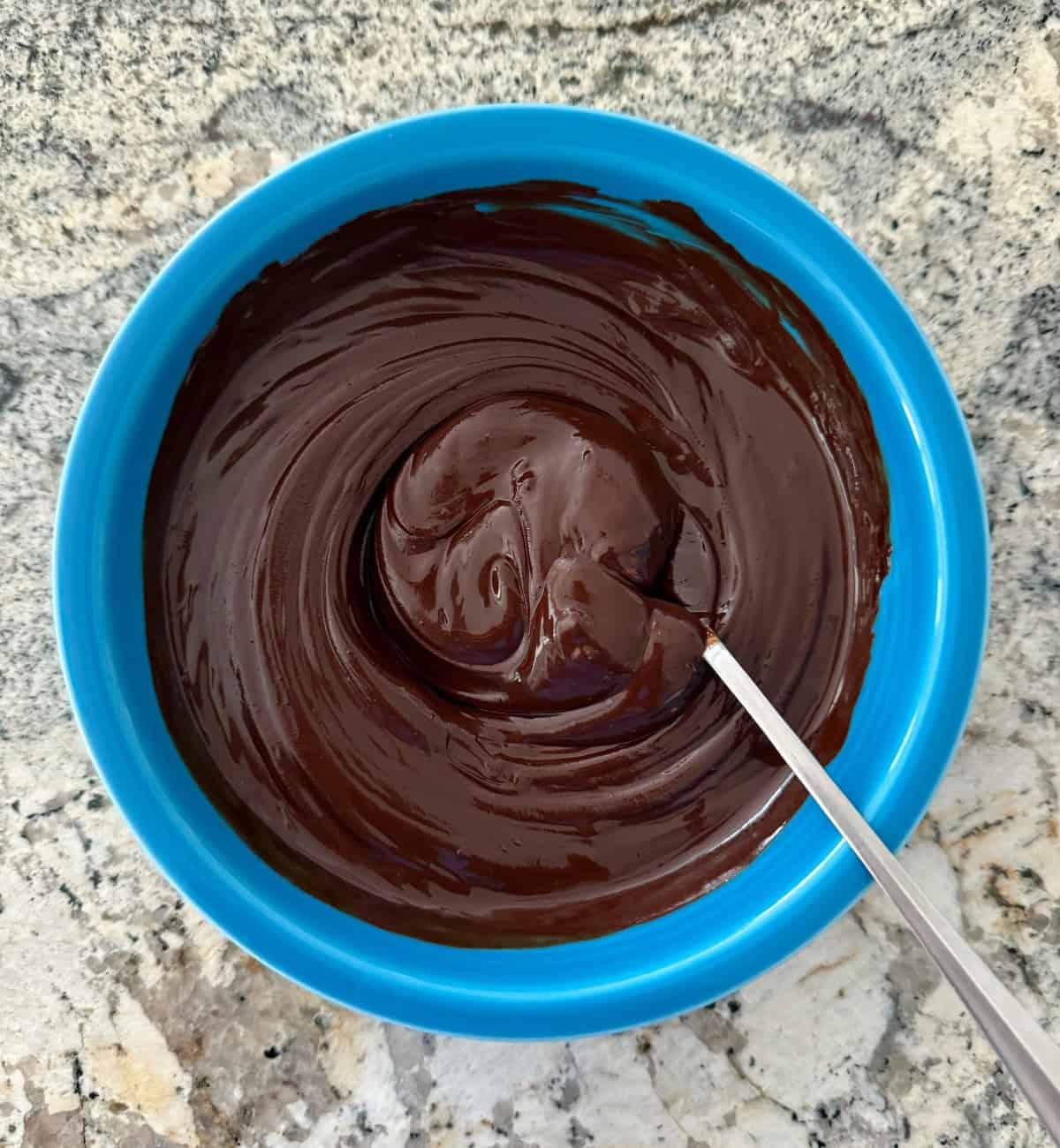 Melted chocolate in blue bowl with spoon.