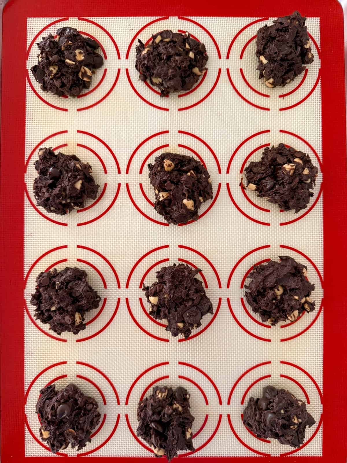 Unbaked chunky chocolate cookies on silicone lined baking sheet.
