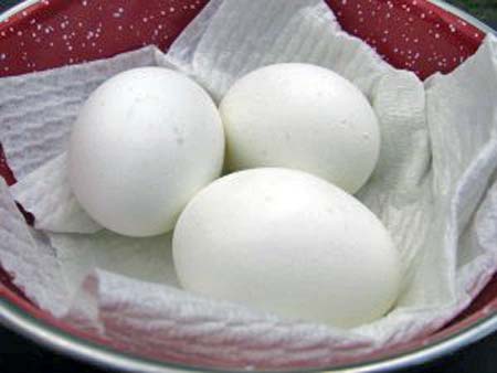 Three hard-boiled eggs on a paper towel in a red bowl