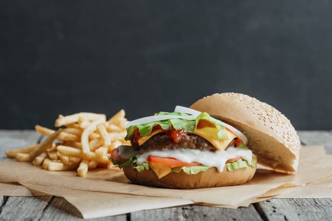 Cheeseburger with lettuce, ketchup with french fries on brown baking paper sitting on a wood table