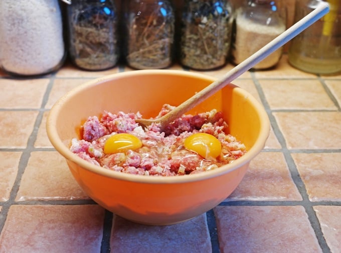 Mixing simple meatloaf ingredients in a yellow bowl with a wooden spoon.