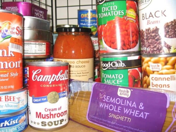 Well-stocked pantry shelf with cans and jars of food and a package of dry pasta