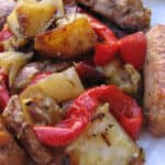 Sausage, peppers, onions and potatoes up close on white plate.