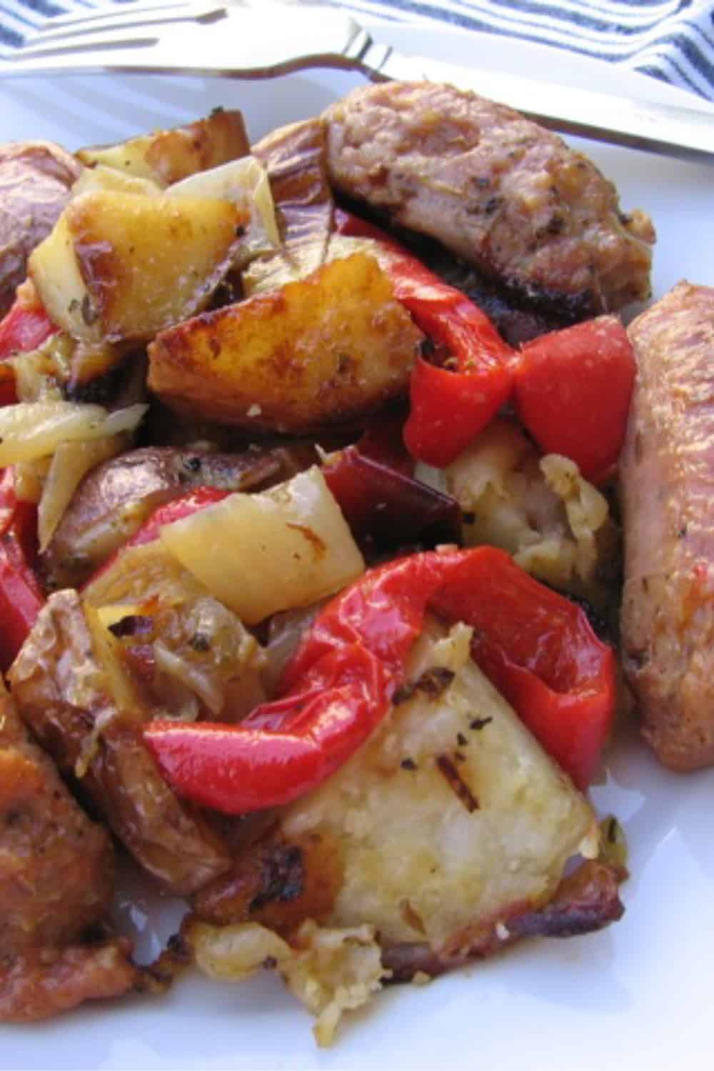 Sausage, peppers, onions and potatoes up close on white plate.