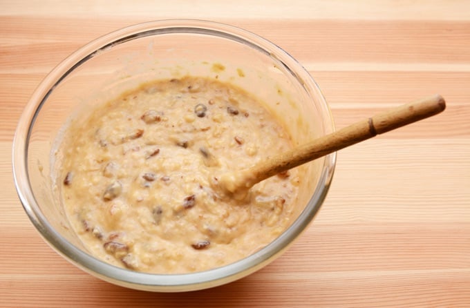 Prepared batter for banana loaf in a glass bowl with a wooden spoon.