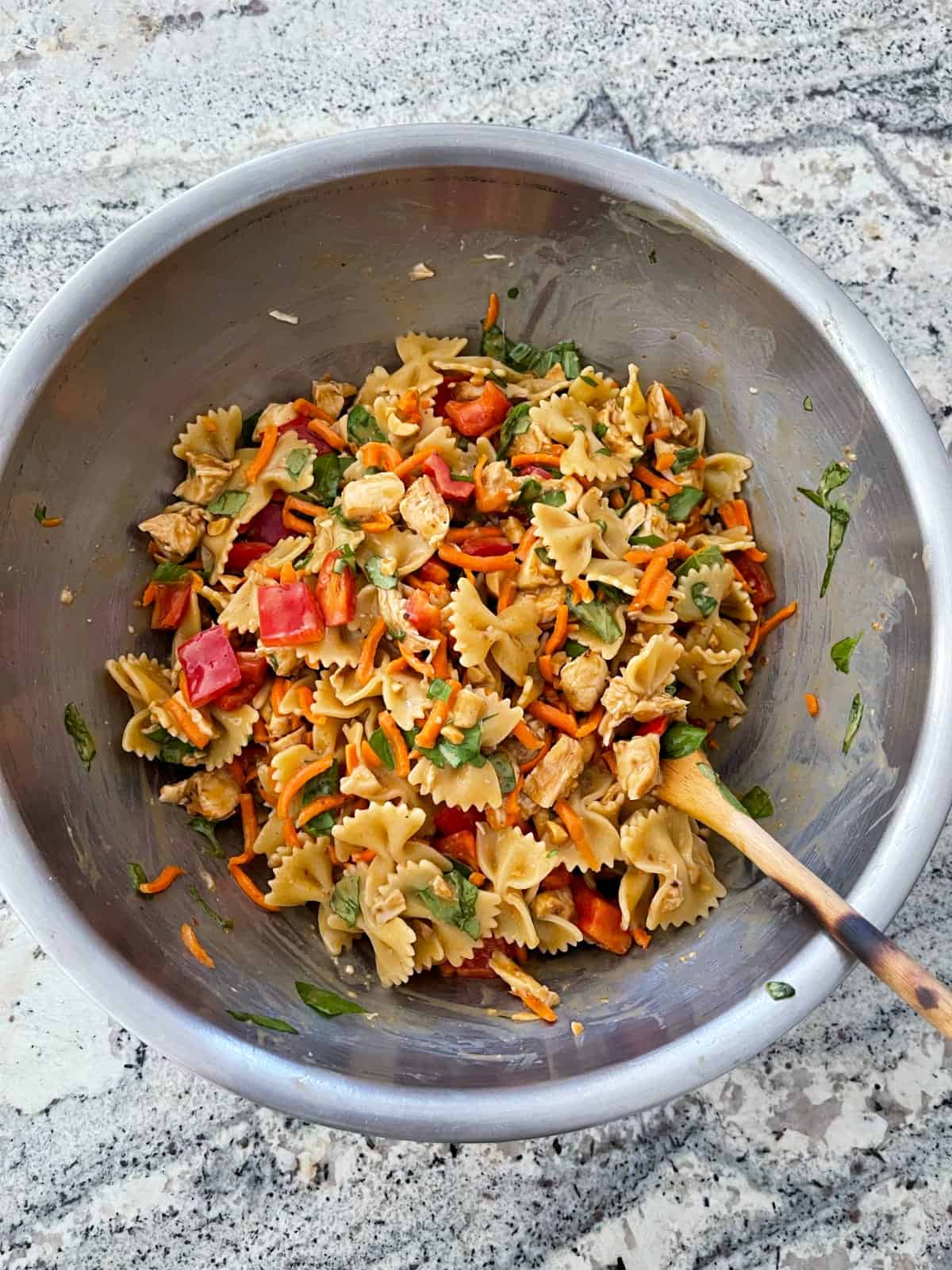 Mixing chicken satay pasta salad in mixing bowl with wooden spoon.