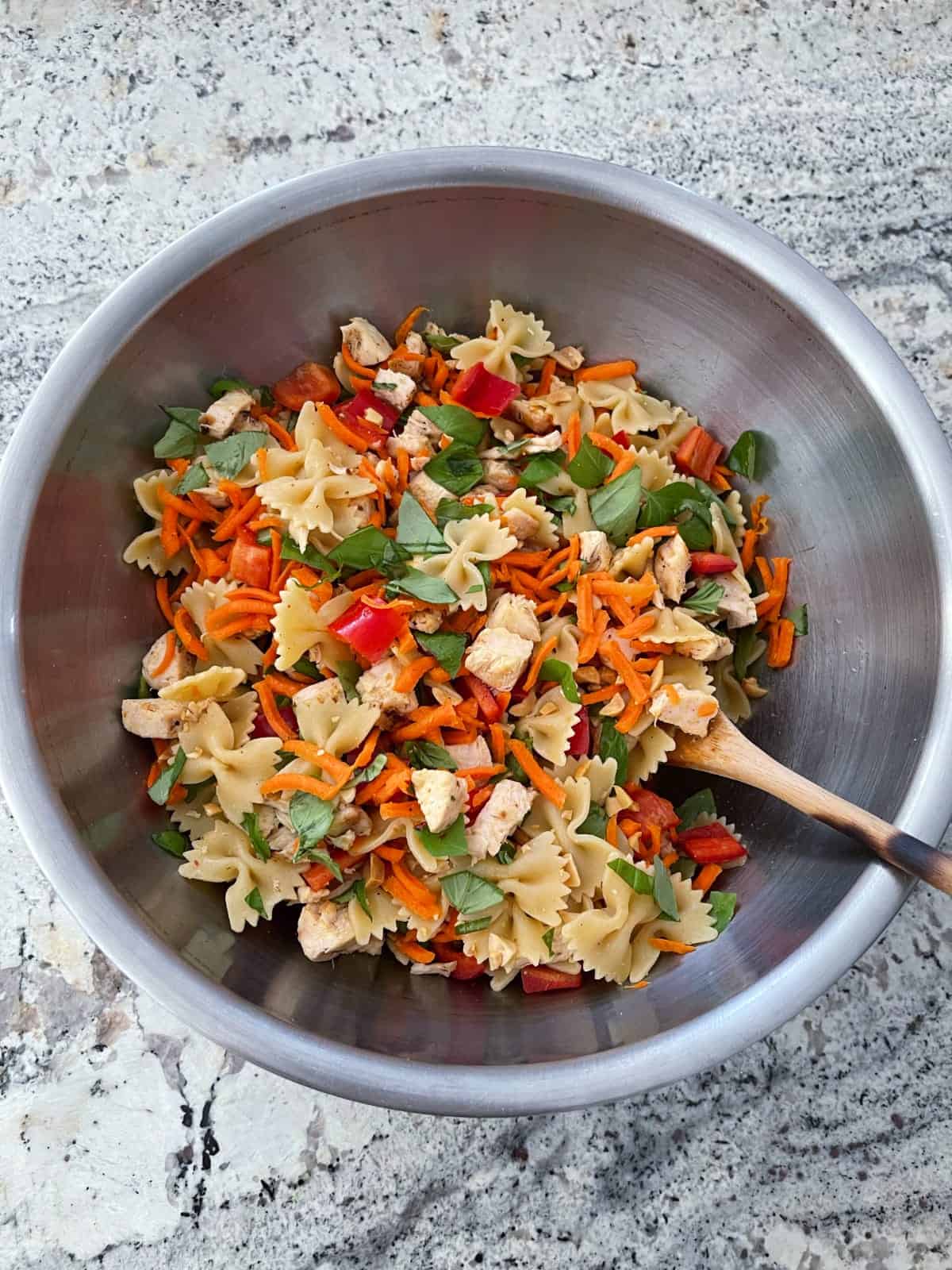 Mixing pasta, chopped basil, red bell pepper, shredded carrots and chopped peanuts in mixing bowl.