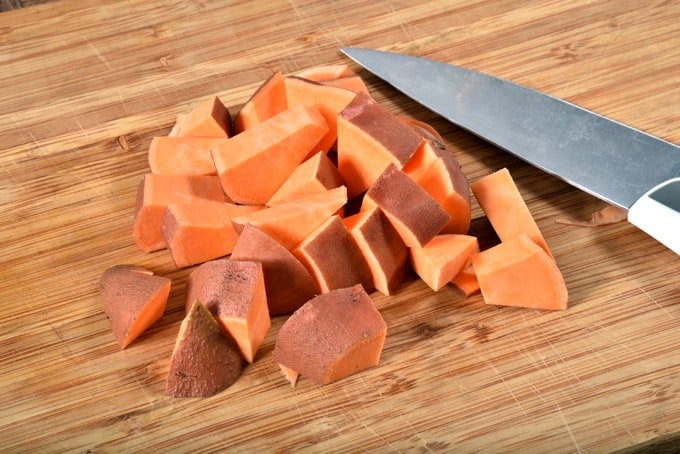 A mound of diced sweet potatoes on a cutting board with a knife.