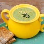 Cream of Broccoli Cheese Soup in a bright yellow crock sitting on a green placemat with toast alongside
