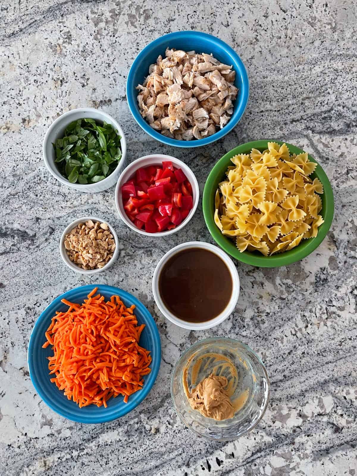 Ingredients including diced chicken breast, chopped basil, dry pasta, chopped red pepper, peanuts, shredded carrots and peanut dressing.