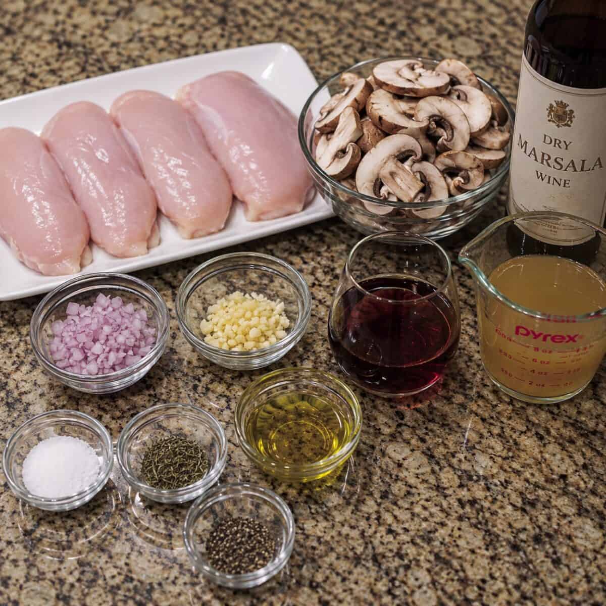 Boneless, skinless chicken breasts, sliced mushrooms, minced garlic, finely chopped shallot, dry Marsala wine, chicken broth, olive oil, salt and pepper on a granite counter.
