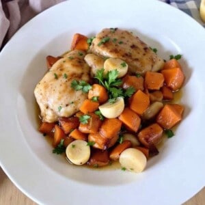 cider braised chicken thighs with sweet potatoes and shallots white shallow plate from above