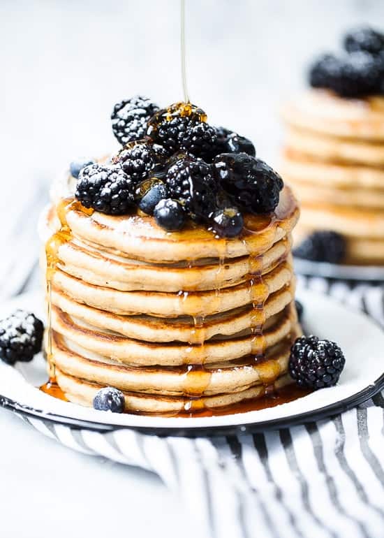 A stack of whole wheat pancakes topped with blackberries, blueberries and drizzled with maple syrup
