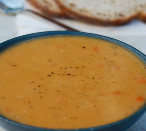 Slow Cooker Yellow Split Pea Soup in blue bowl with sliced bread in the background