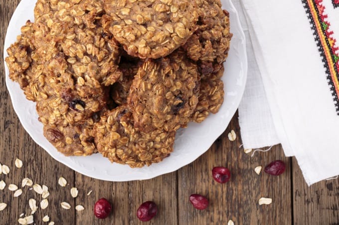 Plate of cranberry oatmeal cookies on a wooden table scattered with dried oats and cranberries