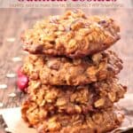 Four cranberry apple oatmeal cookies stacked on top of each other on wooden table with oats and cranberries scattered about.