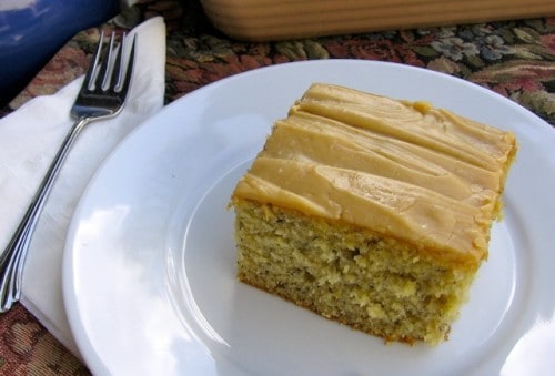 Piece of banana cake with peanut butter frosting on white plate with fork.