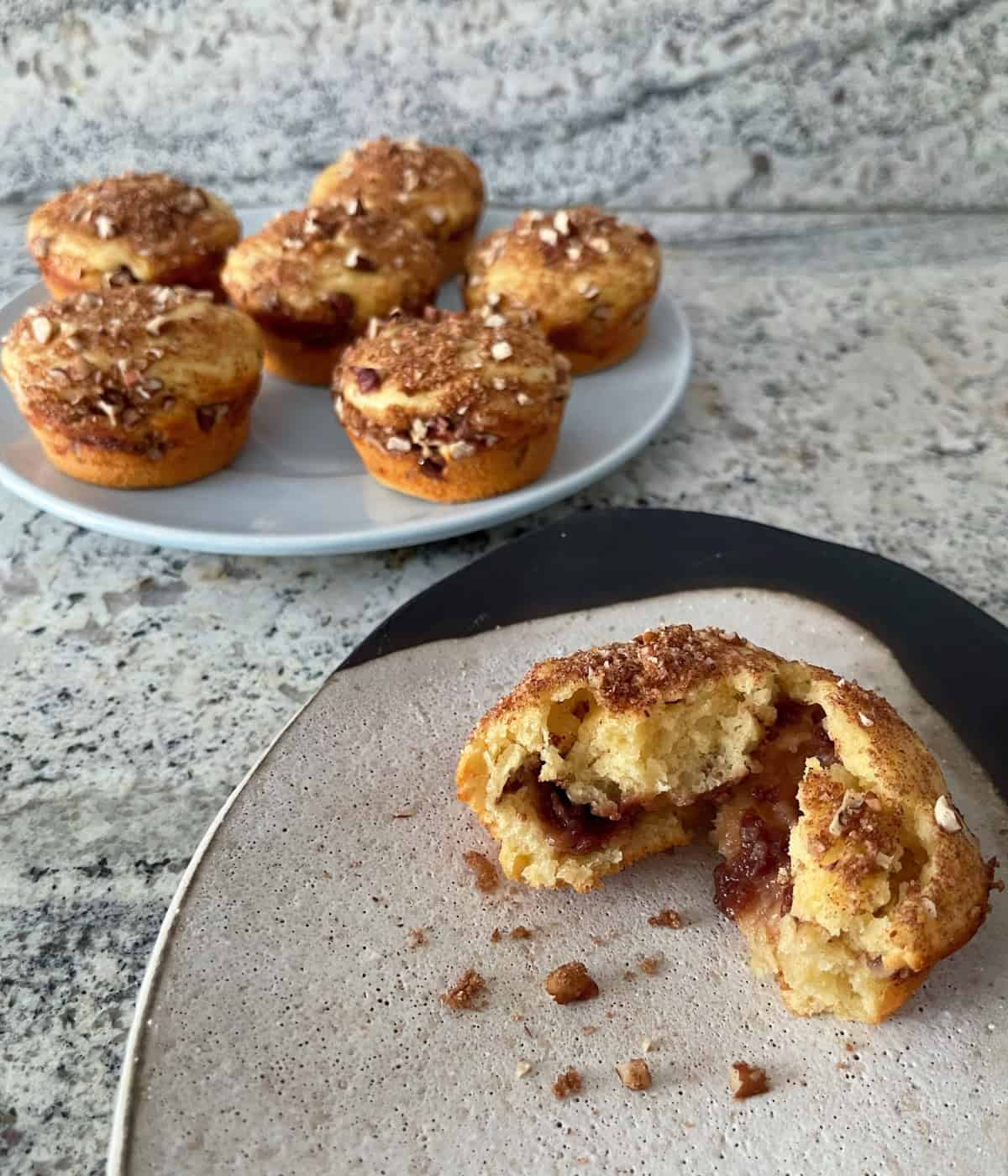 Raspberry cinnamon streusel muffin on small plate with six muffins on larger platter in the back.