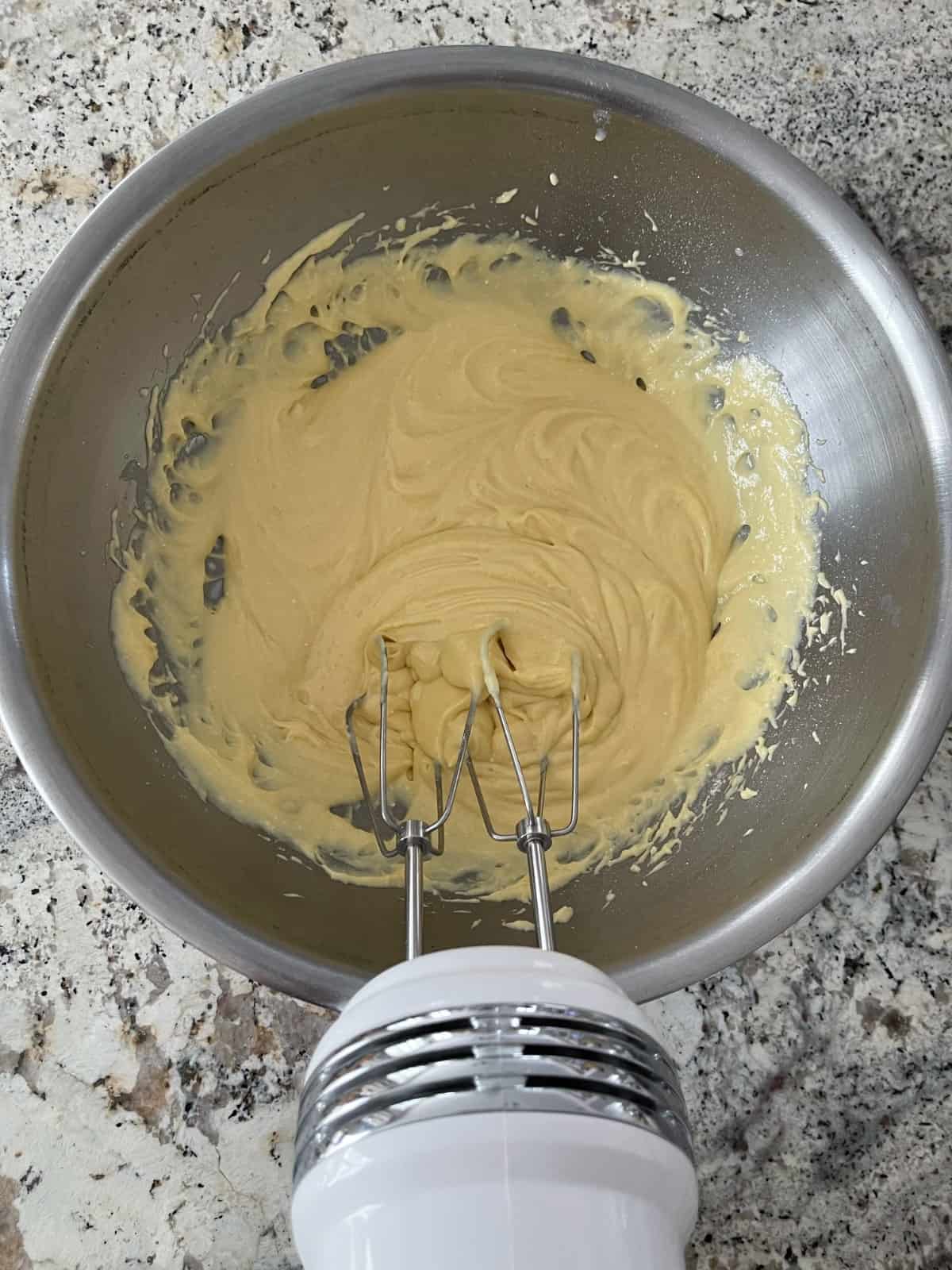 Mixing yellow cake with egg, Greek yogurt, canola oil and vanilla in a mixing bowl with handheld electric mixer.