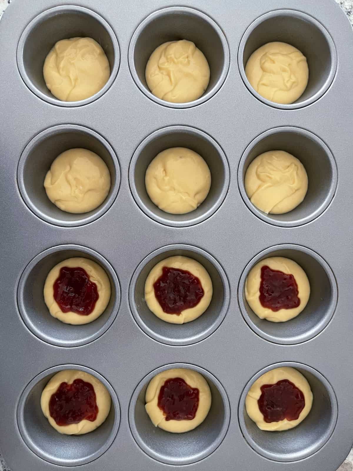 Muffin tin filled with batter and 6 cups topped with 1 teaspoon raspberry fruit spread.
