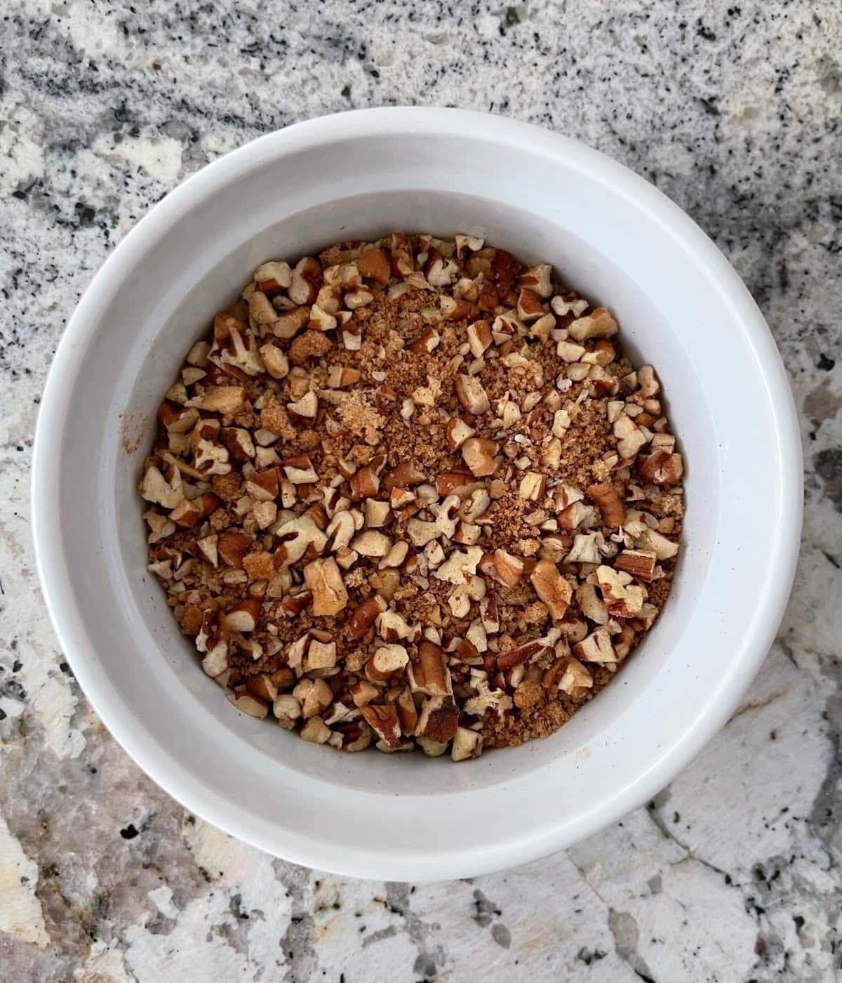Streusel topping mixture of chopped pecans, cinnamon and brown sugar in a small white ramekin.
