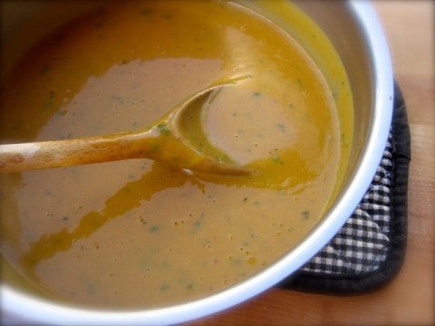 Stirring Curried Sweet Potato Soup with wooden spoon in soup pot.