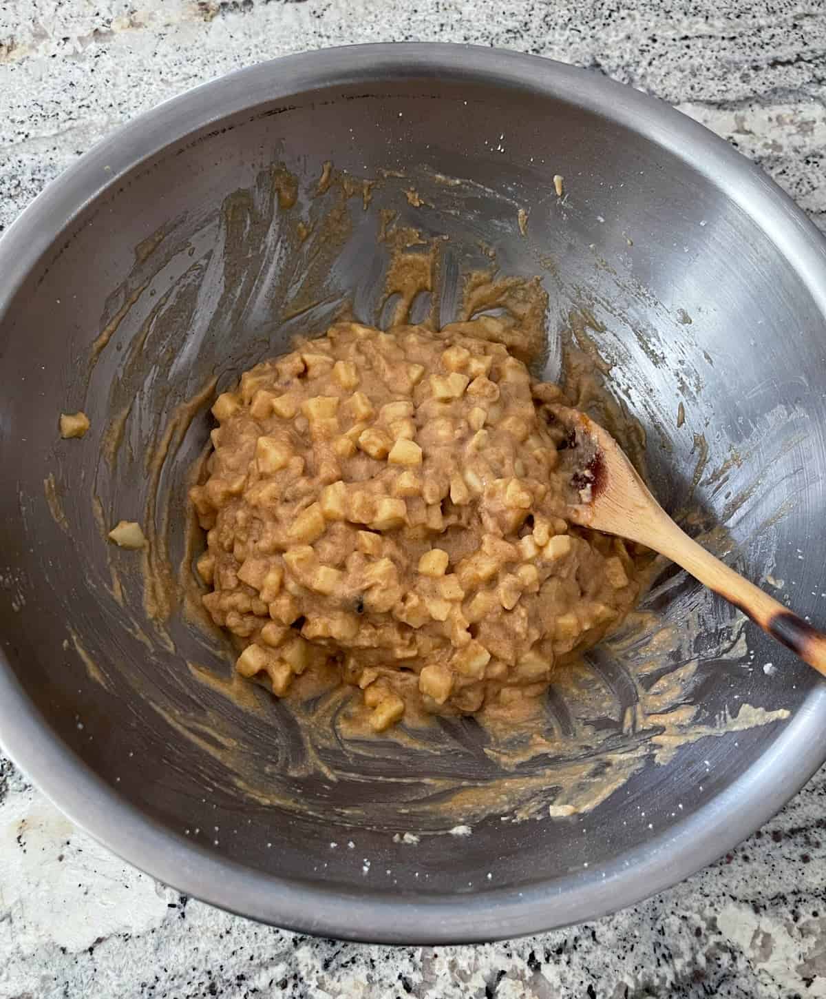 Mixing together apple brownie nut bar batter in a mixing bowl with a wooden spoon.